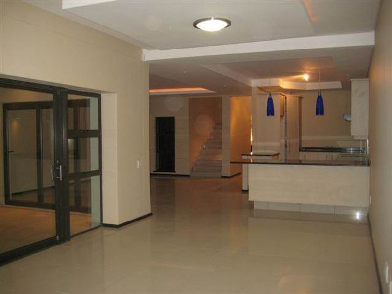 Spacious open-plan living and kitchen area featuring tiled floors, a central kitchen island, recessed ceiling lighting, and large sliding glass doors.