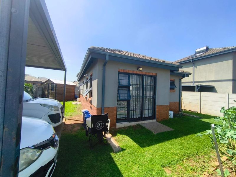 Rear view of the property featuring a brick and plaster facade, tiled roof, security gates, and a private garden area with a carport.