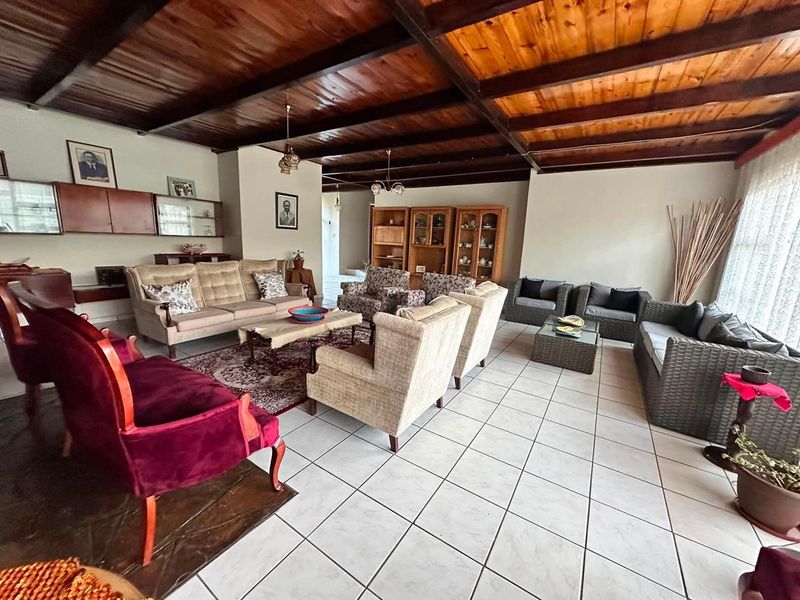 Spacious living room featuring a distinctive exposed timber beam ceiling and neutral ceramic floor tiles, offering a versatile layout for comfortable family living.