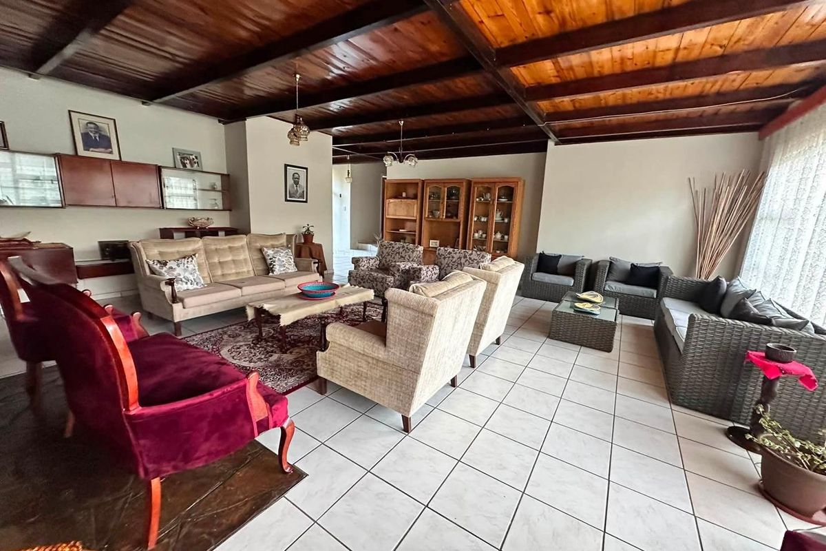 Spacious living room featuring a distinctive exposed timber beam ceiling and neutral ceramic floor tiles, offering a versatile layout for comfortable family living.