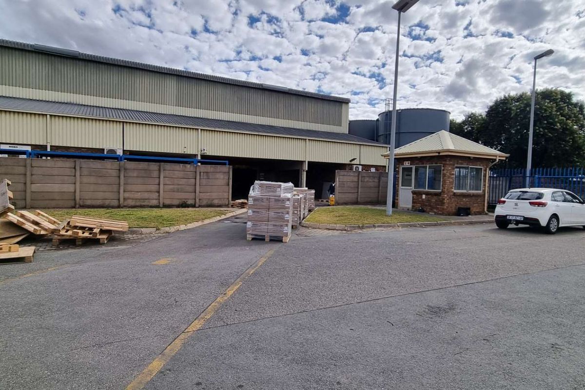Commercial property exterior featuring a large warehouse structure, paved yard area, security guard house, and perimeter fencing.