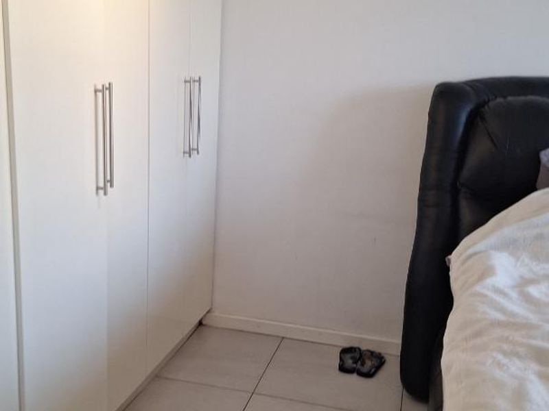A bedroom featuring neutral tiled flooring and modern white built-in cupboards providing ample storage space.