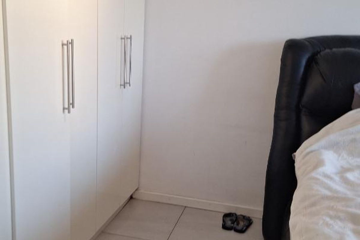 A bedroom featuring neutral tiled flooring and modern white built-in cupboards providing ample storage space.