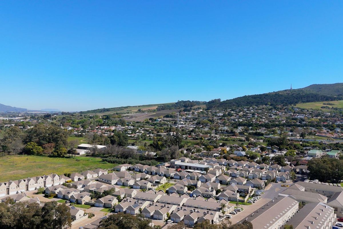 An elevated aerial view showcasing the residential apartment complex and surrounding landscape, including nearby hills and suburban development.