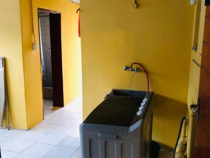 A functional laundry area featuring tiled flooring, a utility sink, and exposed plumbing fixtures.