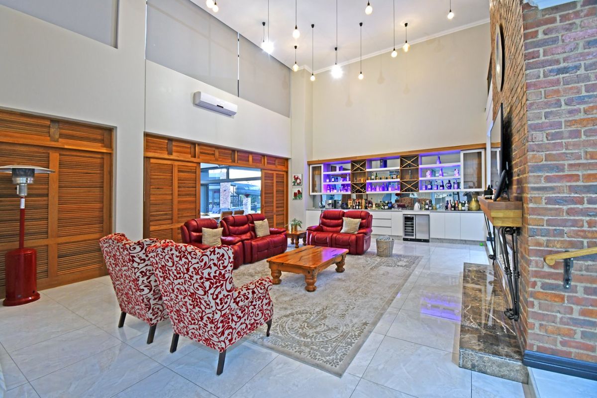 Spacious double-volume living room featuring an exposed brick fireplace, marble hearth, and a custom built-in bar area with integrated wine storage and tiled flooring.