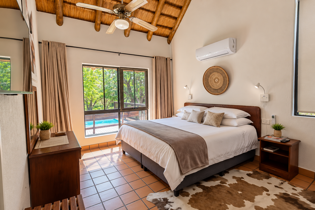 A well-maintained bedroom featuring a high thatched ceiling with exposed timber rafters, tiled flooring, and a split-system air conditioner, overlooking a pool area.