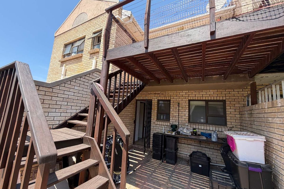 Rear exterior view featuring a paved courtyard area, brick facade, and a raised timber deck with an external staircase.