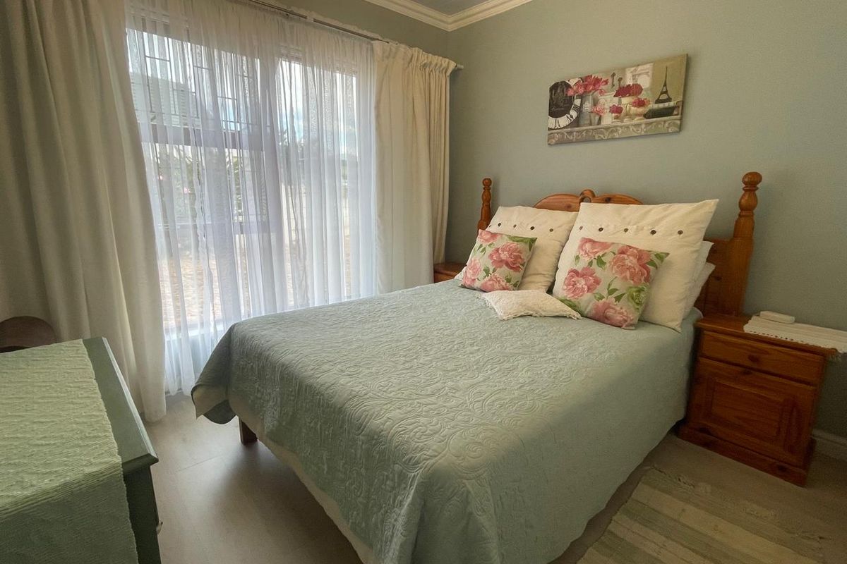 A cozy bedroom featuring light-toned flooring, crown molding, and a large window with sheer curtains, providing ample natural light.