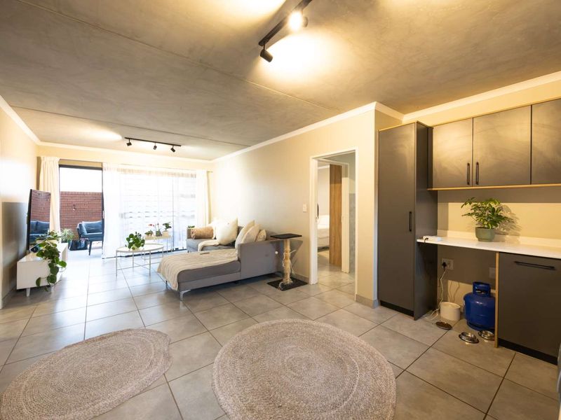 Open-plan living area featuring tiled floors, an exposed concrete ceiling with track lighting, and integrated cabinetry, leading to an outdoor patio space.