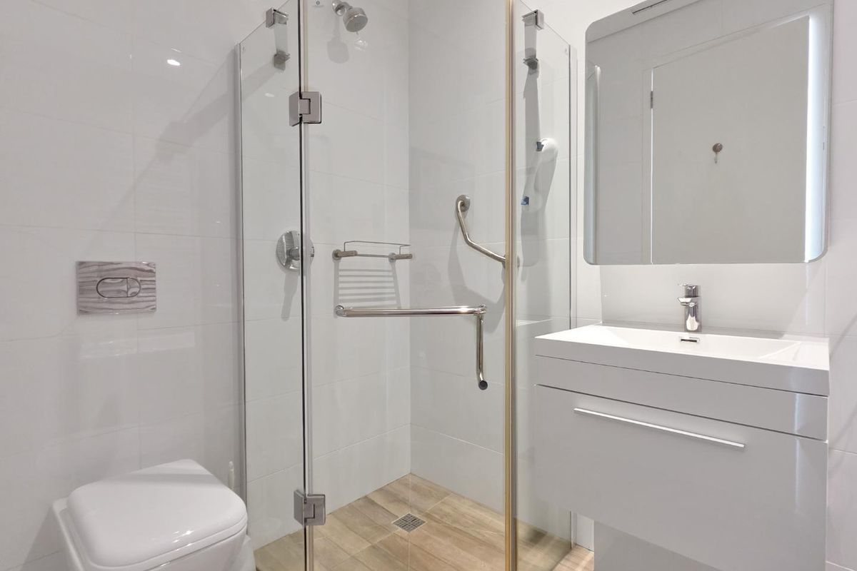 Modern, clean-lined bathroom featuring a wall-hung toilet, glass-enclosed shower with grab rail, and a sleek vanity basin with a wall-mounted mirror.