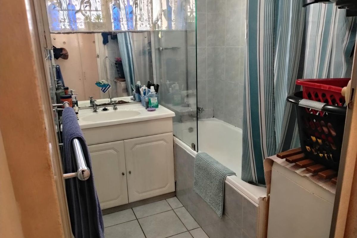 A functional bathroom featuring a vanity cabinet with integrated basin, a bathtub with a glass shower screen, and tiled flooring.