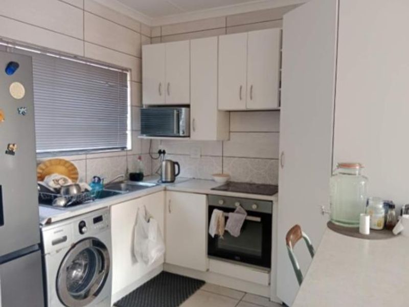 Compact kitchen featuring white cabinetry, tiled backsplash, integrated oven and hob, and dedicated space for laundry appliances.
