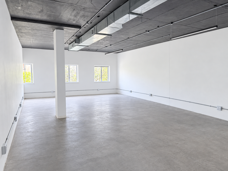 A spacious, modern open-plan office featuring polished concrete floors, an exposed industrial ceiling with HVAC ducting, and clean white walls.