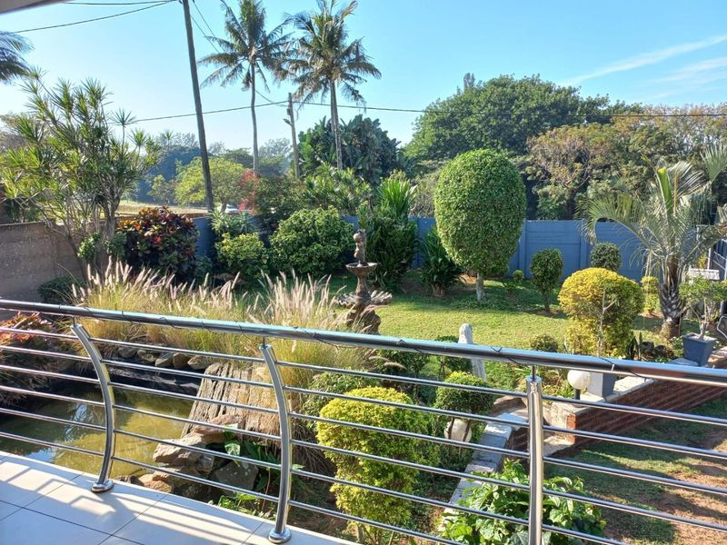 A view from a balcony overlooking a well-maintained garden featuring a water feature, lush landscaping, and a modern stainless steel balustrade.