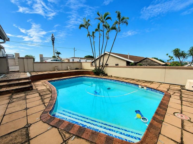 Outdoor pool area featuring a swimming pool with tiled surround, brick coping, and boundary walling.