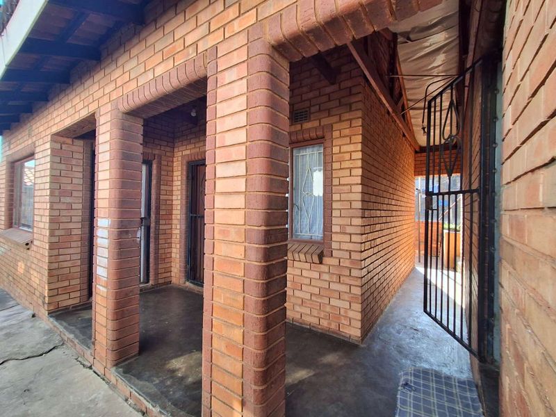 A covered patio area featuring face brick pillars, exposed timber rafters, and secure metal gates, providing a functional outdoor transition space.