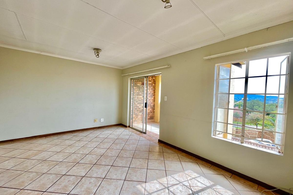 An empty living room featuring tiled flooring, large windows, and a sliding glass door providing access to an outdoor patio area.