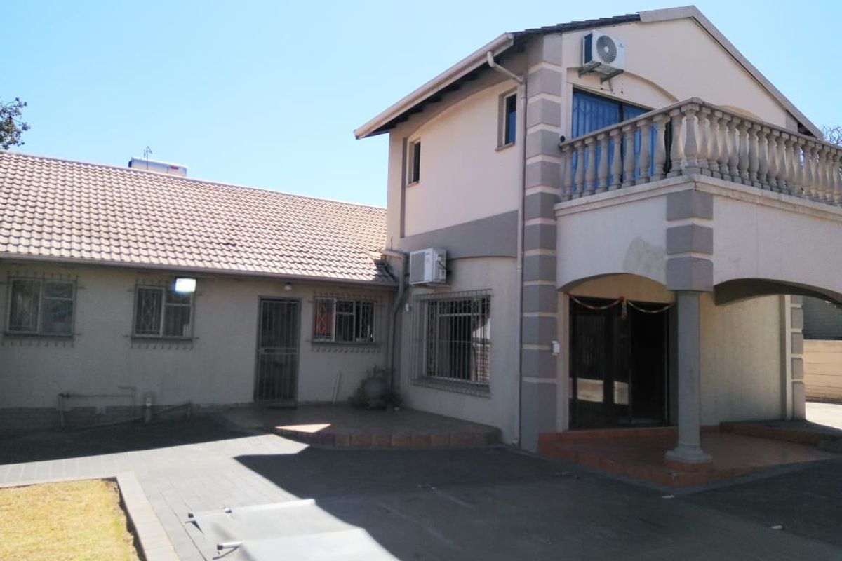 Rear view of a two-story house featuring a paved driveway, a balcony with balustrades, solar water heating, and security bars on windows.