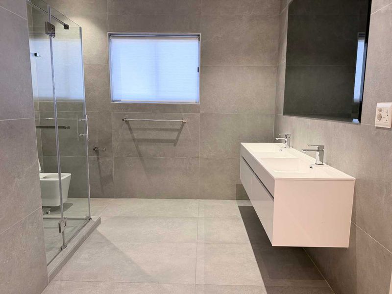 Modern bathroom featuring a sleek double vanity, large format grey tiling, and a spacious glass-enclosed shower.