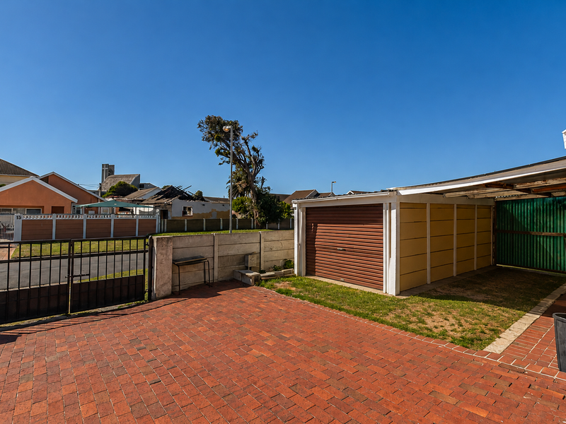Front exterior view featuring a brick-paved driveway, a single garage, and an attached carport with metal fencing and boundary walling.