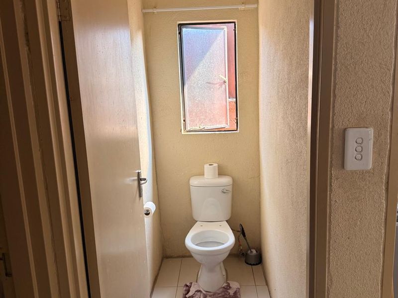 A compact guest toilet featuring tiled flooring and a small window, requiring cosmetic updates to improve the overall finish and appeal.