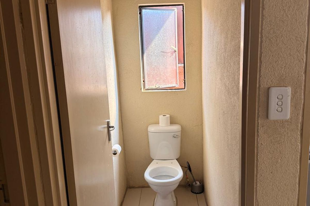A compact guest toilet featuring tiled flooring and a small window, requiring cosmetic updates to improve the overall finish and appeal.