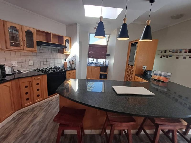 A functional kitchen featuring wooden cabinetry, granite countertops, a gas hob, built-in oven, and a central island with breakfast bar seating.