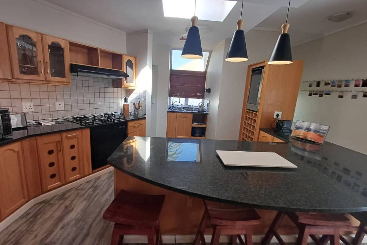 A functional kitchen featuring wooden cabinetry, granite countertops, a gas hob, built-in oven, and a central island with breakfast bar seating.