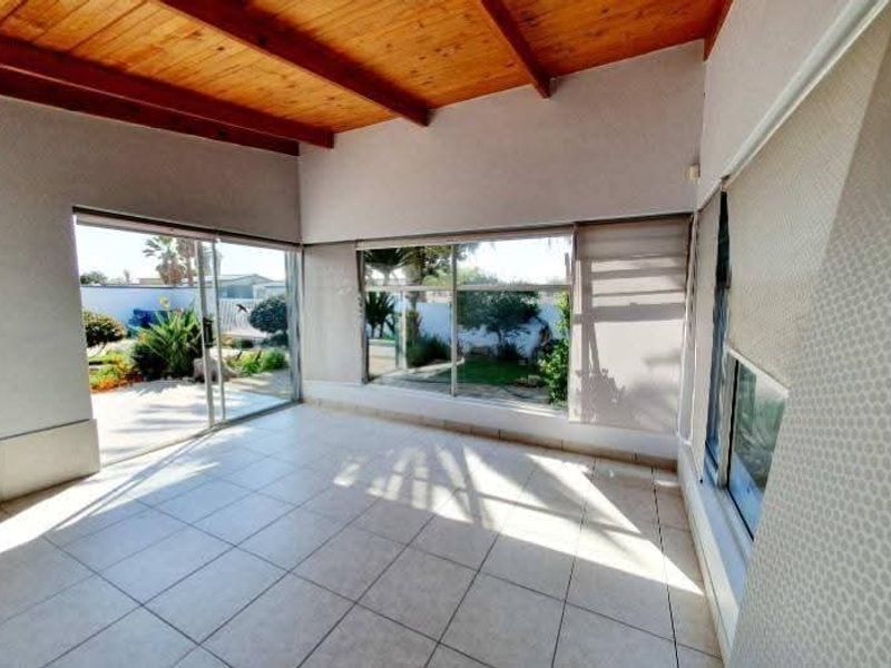 Bright and spacious living area featuring exposed timber beam ceilings, tiled flooring, and large sliding glass doors providing direct access to the garden.