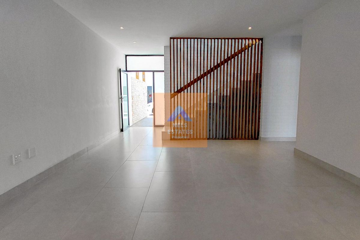 A bright, open-plan living area featuring modern tiled flooring, recessed lighting, and a decorative timber slat screen partition by the staircase.