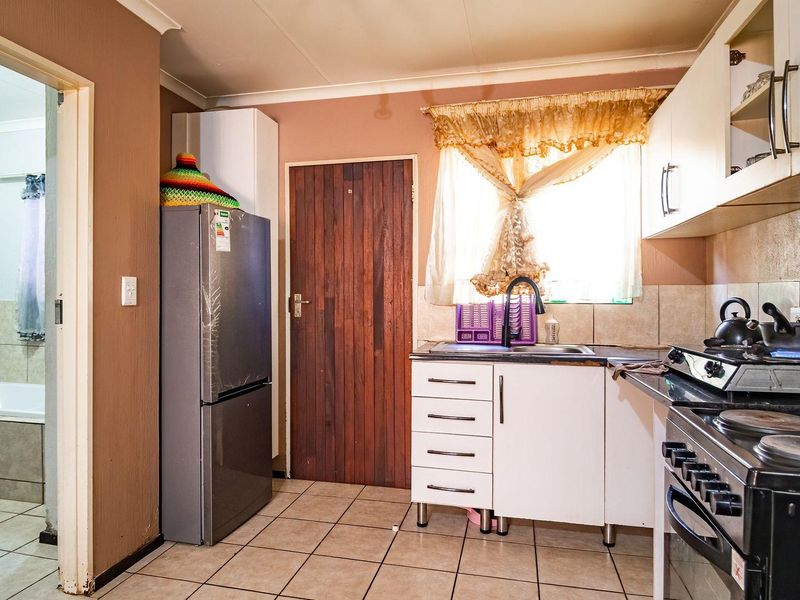 A functional kitchen featuring tiled flooring, built-in cabinetry, and a stove, with an adjacent view into a tiled bathroom area.