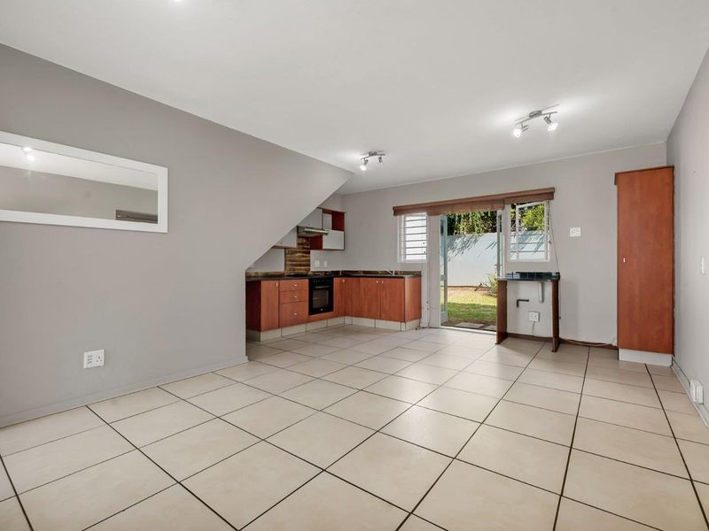 An open-plan living and kitchen area featuring tiled floors, built-in cabinetry, and direct access to a rear garden through a sliding glass door.