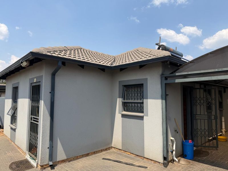 Rear exterior view of the house featuring a tiled roof, solar geyser, paved patio area, and secure metal entrance gates.