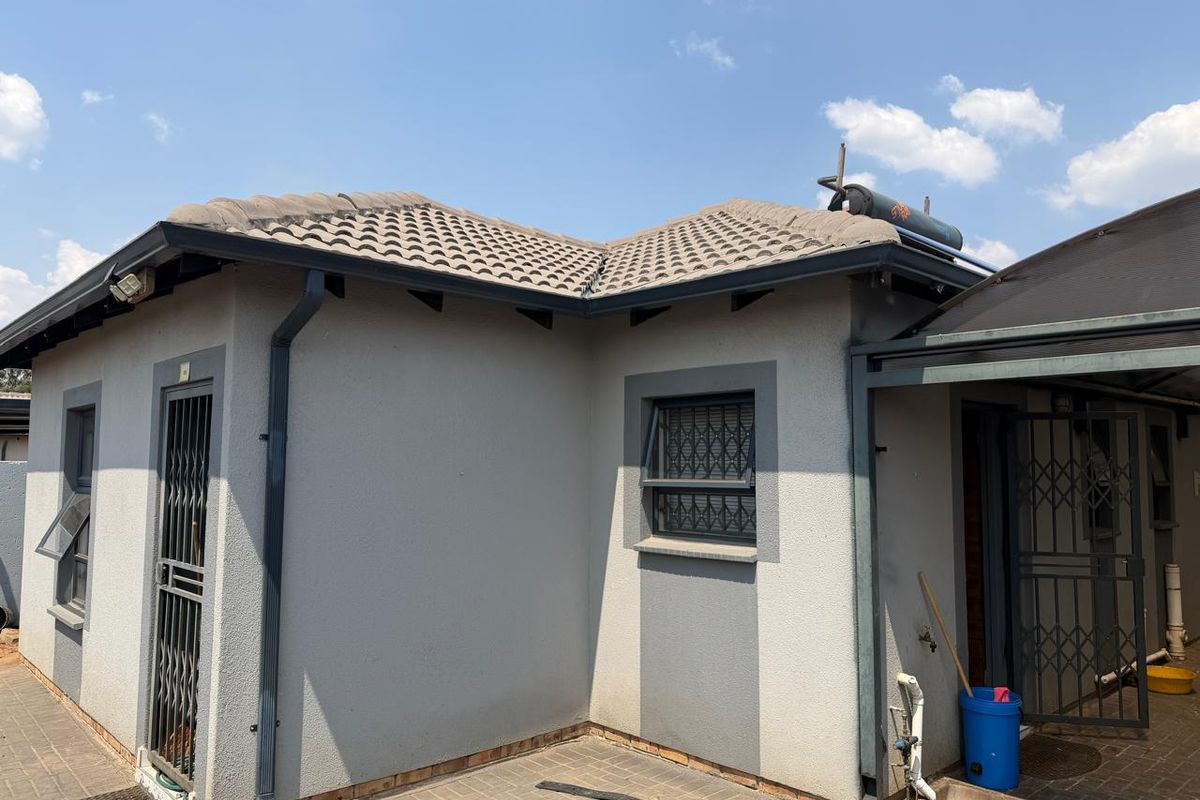Rear exterior view of the house featuring a tiled roof, solar geyser, paved patio area, and secure metal entrance gates.