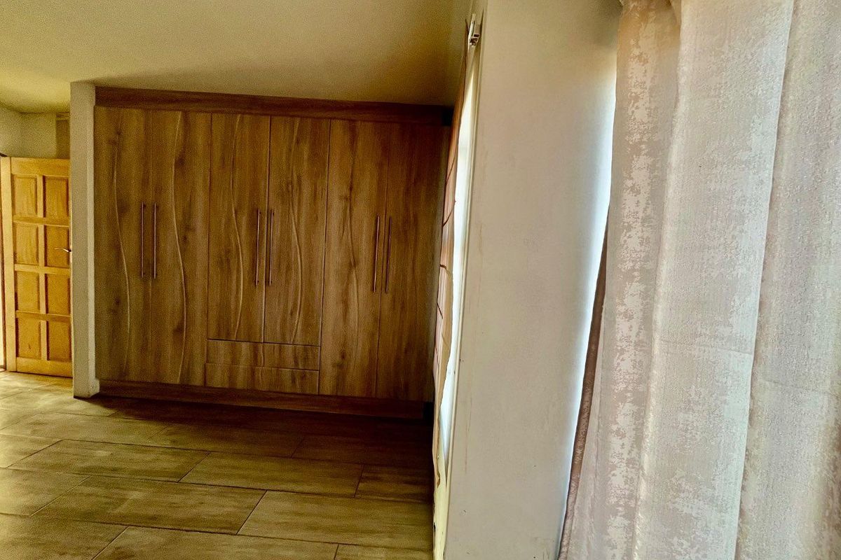 A bedroom featuring built-in wooden cupboards and tiled flooring, offering a clean, neutral space ready for personalization.