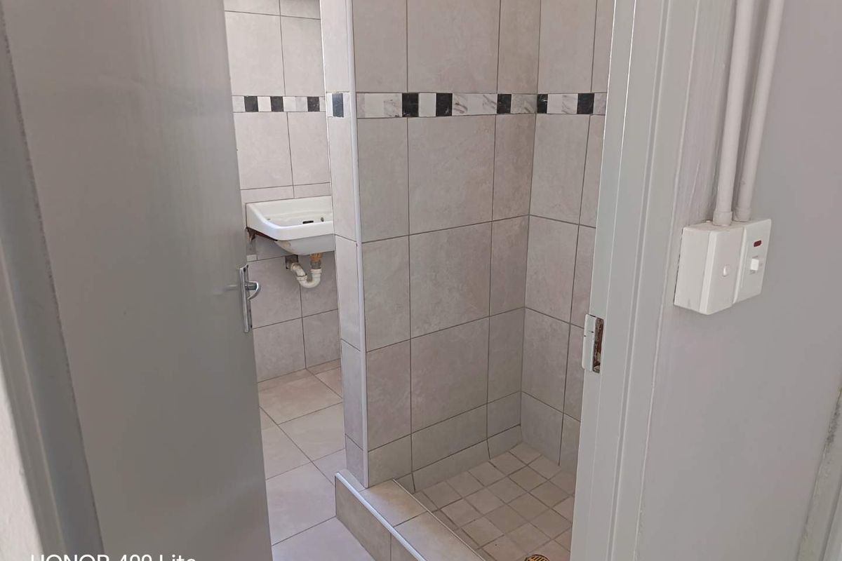 A functional bathroom featuring a tiled shower enclosure and a wall-mounted basin with neutral ceramic wall and floor tiling.