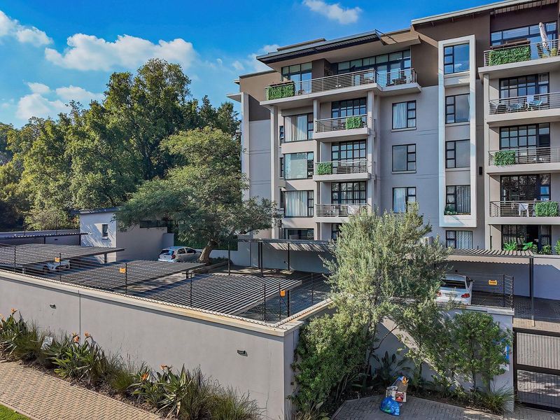 A modern multi-story apartment complex featuring private balconies, covered parking facilities, and secure perimeter walling with gated access.