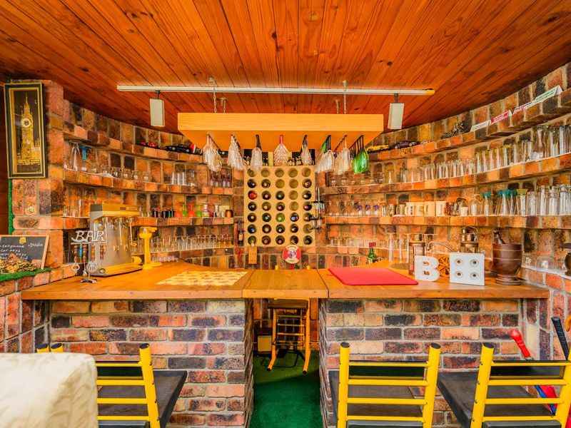 A dedicated home bar area featuring a rustic brick counter, timber-clad ceiling, and integrated glass shelving with a built-in wine rack.
