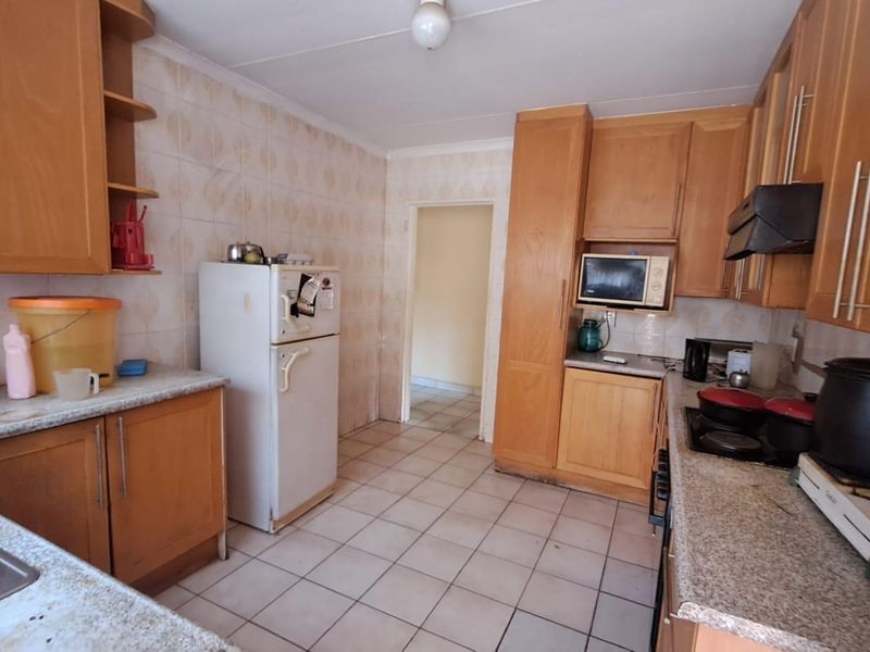 A functional kitchen featuring wood-look laminate cabinetry, granite-style countertops, and ceramic tile flooring, offering a dated aesthetic ready for modernization.