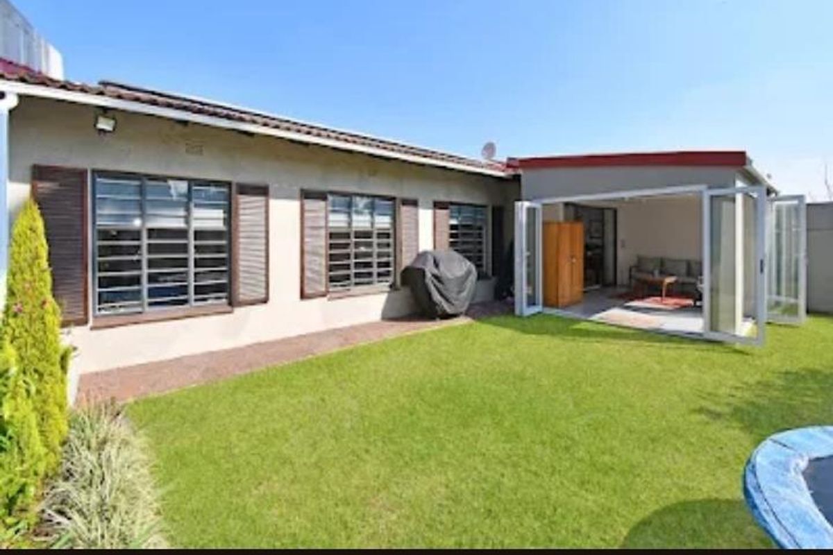 Rear view of the property featuring a well-maintained lawn, covered patio area with folding stacker doors, and aluminium window frames.