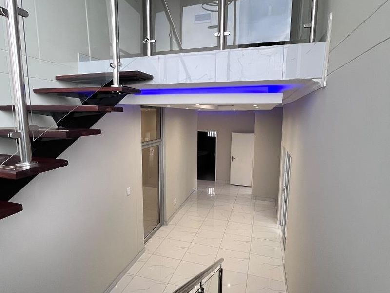 Modern hallway featuring a floating staircase with glass balustrades, stainless steel handrails, polished porcelain floor tiles, and integrated LED accent lighting.