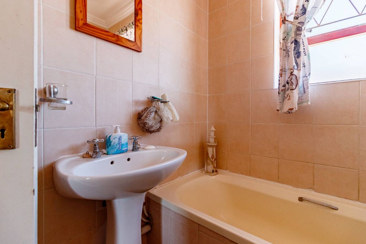 A functional bathroom featuring a pedestal basin, built-in bathtub, and neutral ceramic wall tiling.