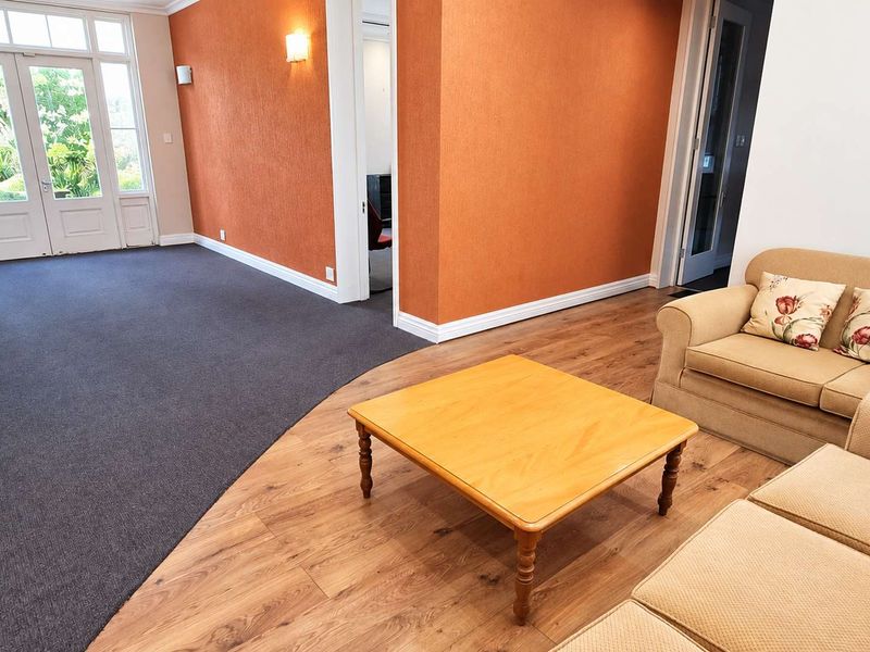 Spacious office area featuring a mix of carpet and laminate flooring, bright orange accent walls, and direct access to the exterior via french doors.