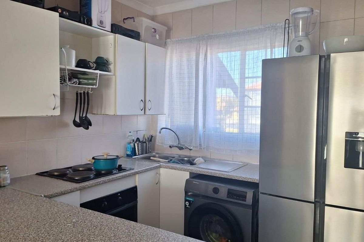 Compact kitchen featuring built-in cabinetry, integrated electric hob and oven, stainless steel sink, and dedicated space for a washing machine.