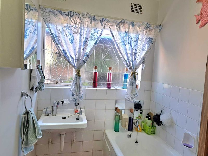 A functional bathroom featuring a wall-mounted basin, built-in bathtub, and tiled splashback, with security bars on the window.