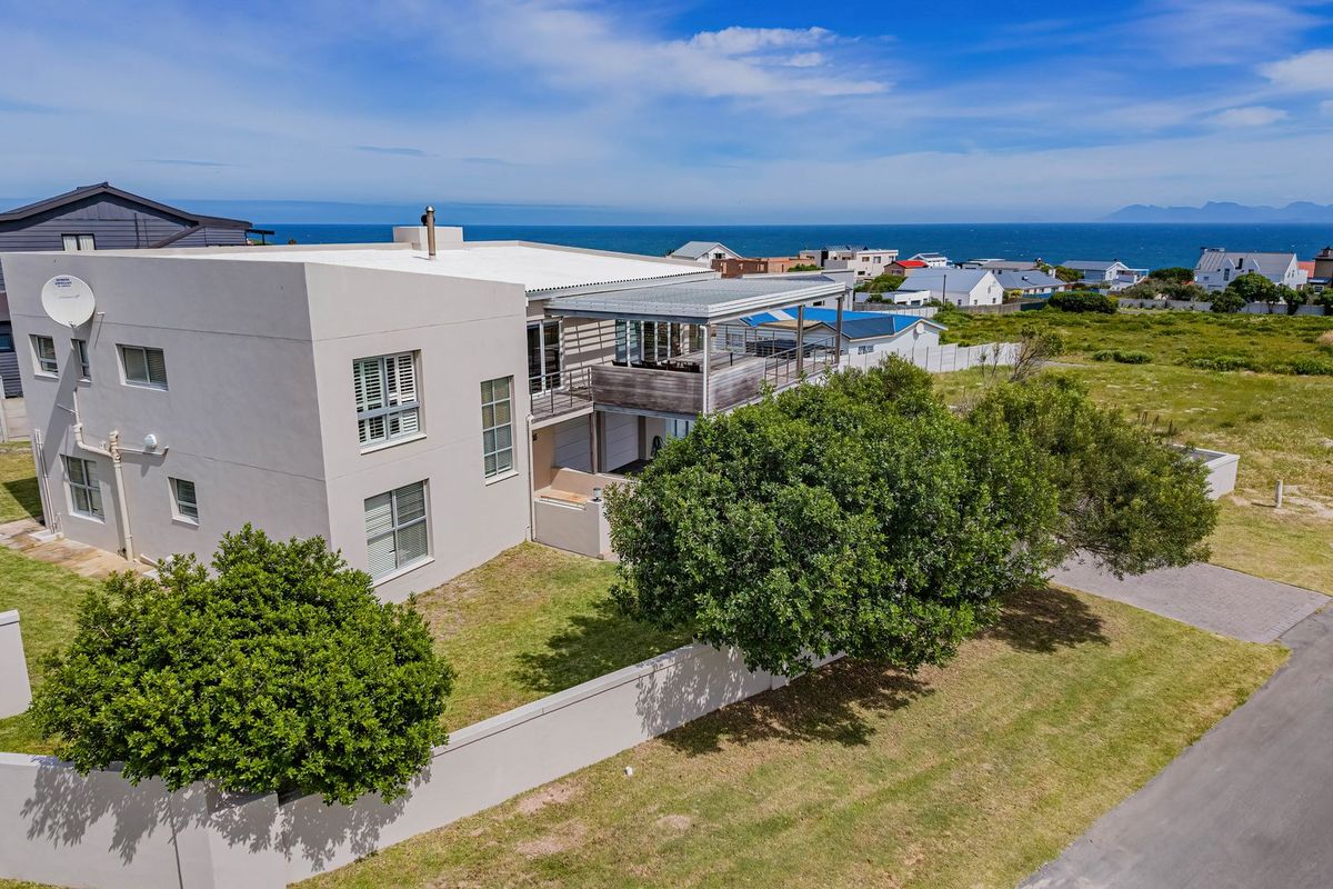 Aerial view of a modern multi-story coastal home featuring a flat roof, balcony, and surrounding garden with boundary walling.