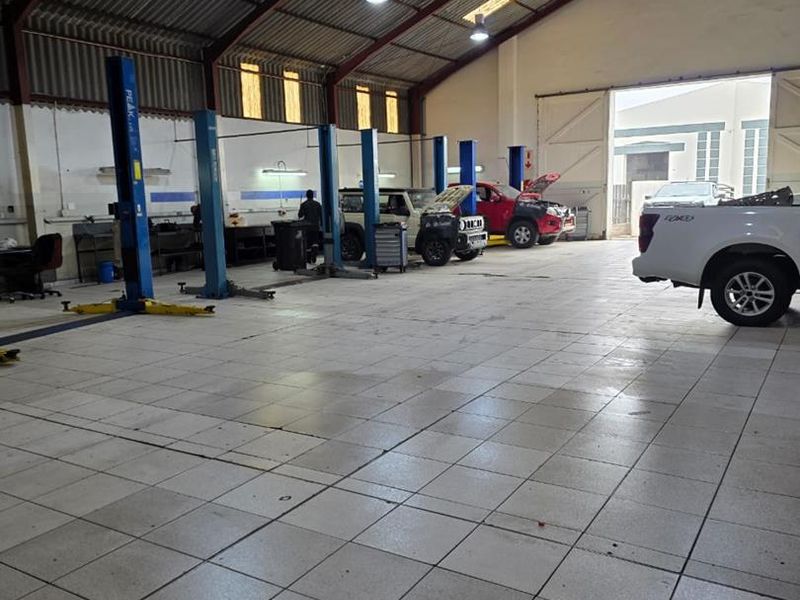 Spacious industrial workshop featuring multiple vehicle lifts, durable tiled flooring, and high-pitched roof with integrated lighting, suitable for automotive service operations.