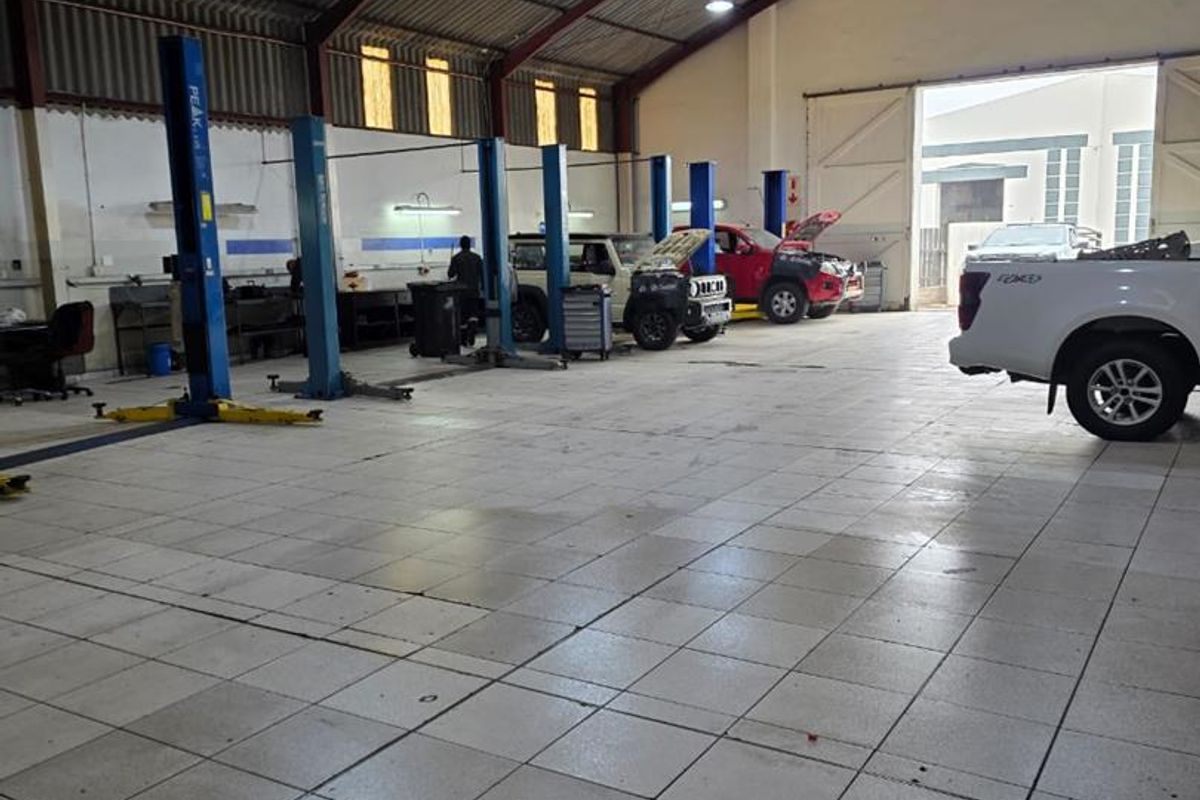 Spacious industrial workshop featuring multiple vehicle lifts, durable tiled flooring, and high-pitched roof with integrated lighting, suitable for automotive service operations.