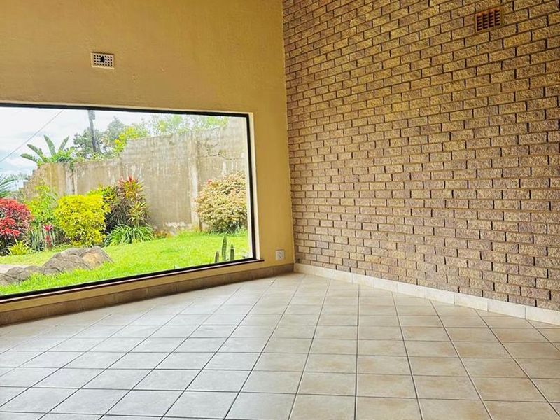 Spacious living area featuring a high exposed timber beam ceiling, a prominent feature brick wall, and large windows overlooking the garden.
